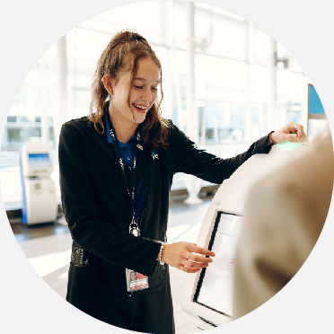 Employé du service à la clientèle accompagnant un passager devant une borne d'enregistrement 